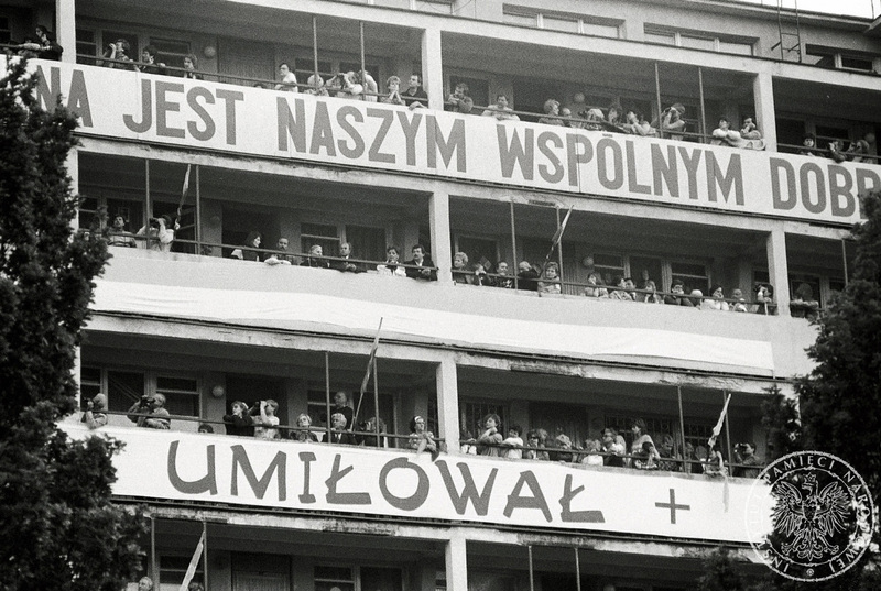 Wierni na balkonach bloku przy Skwerze Kościuszki obserwują spotkanie Jana Pawła II z ludźmi morza. Na balkonach napis „[Ojczyz]na jest naszym wspólnym dobr[em]” i „[Do końca ich] Umiłował” 11 VI 1987 r., Sygnatura: IPNBU-7-7-8-165